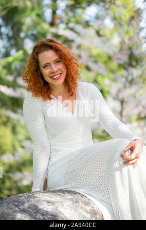 Ritratto di una donna con capelli rossi seduta su una roccia nei Giardini VanDusen; Vancouver, British Columbia, Canada Foto Stock