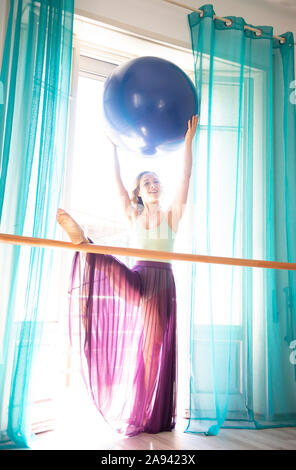 Una ballerina femminile si allunga e pratica davanti ad una finestra in uno studio di danza; Lugano, Ticino, Svizzera Foto Stock