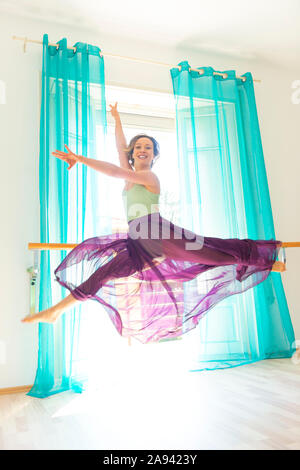 Una ballerina femminile balza in aria in una mossa danzante con una gonna a tulle e guarda la telecamera; Lugano, Ticino, Svizzera Foto Stock