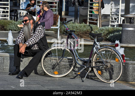 Di Zrenjanin, Serbia, 27 settembre 2019. L'uomo, ciclista appoggiato dalla fontana nel centro cittadino. Foto Stock