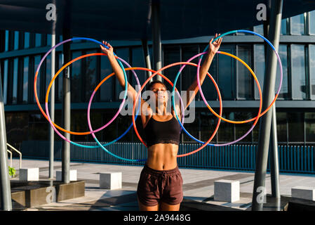 Generazione Z donna giovane azienda cinque hula hoop nel centro cittadino al tramonto Foto Stock