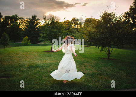 Un ballerino in lungo abito bianco ghirigori nella luce dorata in parco al tramonto Foto Stock