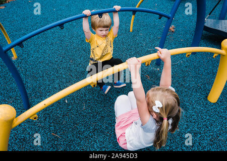 Due bambini swing su una struttura di gioco. Foto Stock