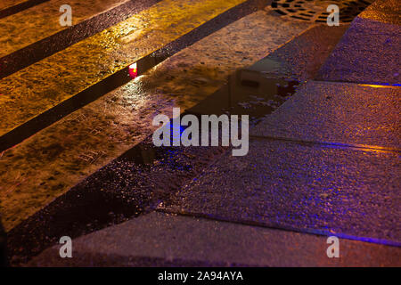 La pozzanghera a crosswalk urban luci notturne. superficie bagnata la riflessione Foto Stock