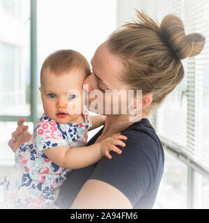 Ritratto della bambina con la madre a casa, madre che bacia il bambino sulla guancia; Vancouver, British Columbia, Canada Foto Stock