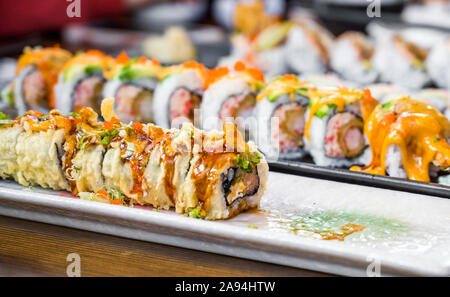 Piastre con vari tipi di sapientemente cotte e fette di sushi con spezie e salse piccanti vengono visualizzate sul tavolo da pranzo per gustare deliziosi e dietetiche Foto Stock