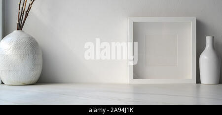 Ritagliato shot di minima area di lavoro con mock up telaio e vasi di ceramica decorazioni su bianco tavolo in legno con spazio di copia Foto Stock