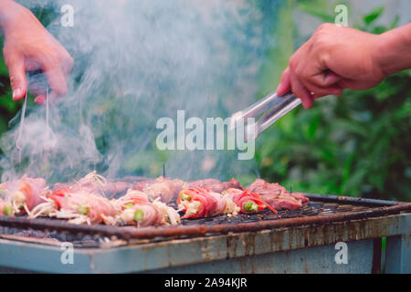 La pancetta avvolto in ago essendo funghi arrosto con carbone di legna sulla griglia. Barbecue funghi alla griglia sulla griglia di acciaio su stufa a carbone bruciata Foto Stock