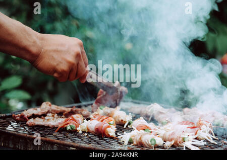 La pancetta avvolto in ago essendo funghi arrosto con carbone di legna sulla griglia. Barbecue funghi alla griglia sulla griglia di acciaio su stufa a carbone bruciata Foto Stock