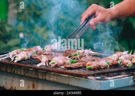 La pancetta avvolto in ago essendo funghi arrosto con carbone di legna sulla griglia. Barbecue funghi alla griglia sulla griglia di acciaio su stufa a carbone bruciata Foto Stock