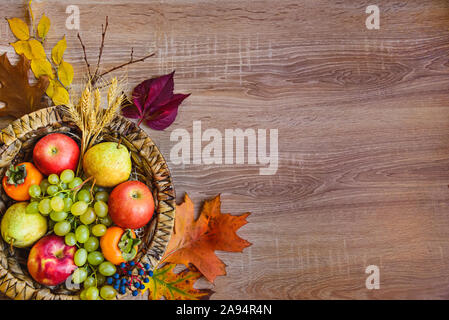 Vista superiore di vari colori d'autunno frutti e foglie in un cesto di vimini su un tavolo di legno. Copia dello spazio. Foto Stock