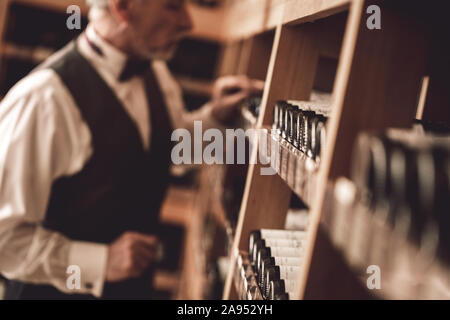 Concetto di sommelier. Senior man standing scelta di varietà di vino di close-up sfondo sfocato Foto Stock
