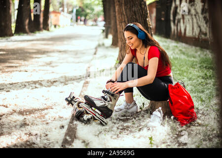 Donna allacciamento rulli mentre seduto nel parco e ascolto di musica con cuffie Foto Stock