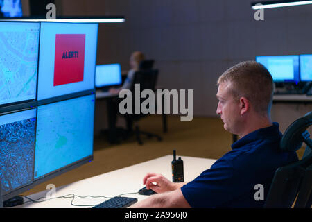 Nella sala di controllo per la sicurezza Officer monitoraggio di più schermi durante la ricezione del segnale di avviso. Foto Stock
