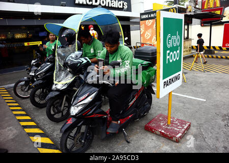 ANTIPOLO City, Filippine - 8 Novembre 2019: driver di un cibo popolare servizio di consegna attendere per gli ordini dei clienti al designato un parcheggio. Foto Stock