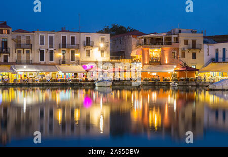 Rethymno, Creta, Grecia. Vista sul porto veneziano al crepuscolo, ristoranti luminosi che si riflettono nell'acqua. Foto Stock