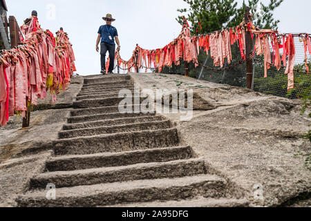 Huashan, Cina - Agosto 2019 : Maschio turistico con un cappello a piedi verso il basso il taglio in una roccia scalini in pietra gradini che portano alla cima di un picco ovest su H Foto Stock