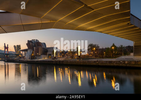 View all'alba attraverso il fiume Nervion verso l'illuminata Museo Guggenheim. Preso dal di sotto della Pasarela Pedro Arrupe bridge, Bilbao, Spagna Foto Stock