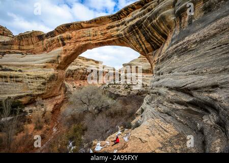 Tourist siede sotto roccia arch, Sipapu Bridge, ponti naturali monumento nazionale, Utah, Stati Uniti d'America Foto Stock