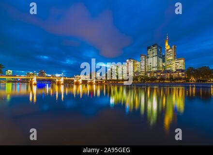 Skyline di Francoforte con i grattacieli illuminati e ponte Untermainbrucke con acqua riflessioni in Main, Schaumainkai, Frankfurt am Main, Hesse Foto Stock