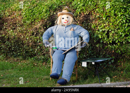 A friendly scarecrow sitting on a chair wearing pyjamas and a straw hat in a rural Wiltshire village scarecrow building competition Foto Stock