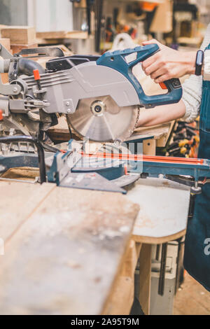 Laboratorio di falegnameria - La ragazza funziona con una barra di legno su una sega a taglio obliquo Foto Stock