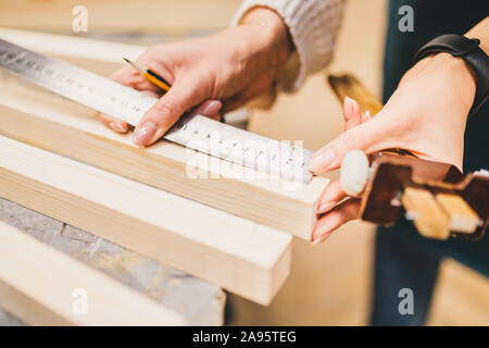 Laboratorio di falegnameria - close-up mani femminili mark bar in legno per tagliare Foto Stock