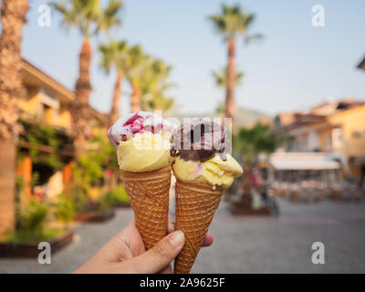 Due porzioni di gelato in un cono di cialda. La ragazza tiene in mano un gelato per due, gelato e sorbetto, frutta e cioccolata Foto Stock