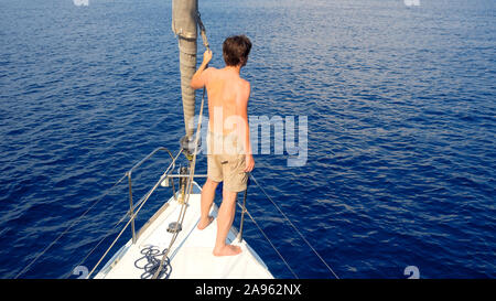 Uomo in pantaloncini corti si erge sul ponte in prossimità della vela, vela e yachting, concetto. Guy su uno yacht viaggio sullo sfondo del mare. Foto Stock
