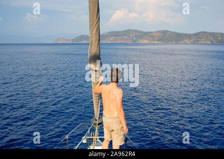 Guardare al di là dell'orizzonte. l uomo in pantaloncini corti si erge sul ponte in prossimità della vela, vela e yachting, concetto. Guy su uno yacht di viaggio. Foto Stock