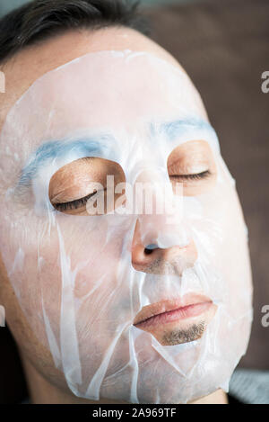 Primo piano di un bel uomo caucasico indossando un bio-foglio di cellulosa mask Foto Stock