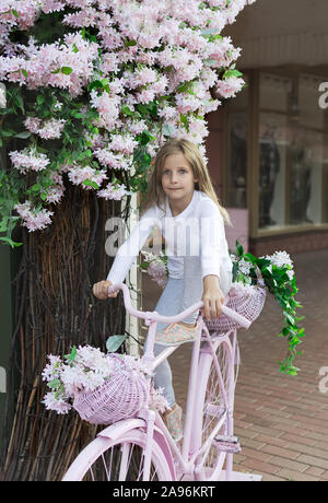 Bambina sulla bicicletta rosa. con un cesto pieno di fiori. Sera d'estate Foto Stock