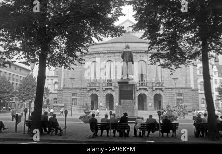 Mainzer sitzen auf Bänken auf dem Gutenbergplatz und blicken auf das Gutenbergdenkmal und das Stadttheater in Mainz, Deutschland 1961. Abitanti di Magonza seduti sui banchi sulla Gutenbergplatz square, rivolto verso la parte posteriore del monumento di Gutenberg e la città del teatro, Germania 1961. Foto Stock