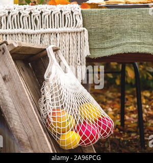 Raccolto autunnale di mele e melograni in una stringa di bianco borsa che si blocca su una vecchia scatola rustico in giardino. Foto Stock