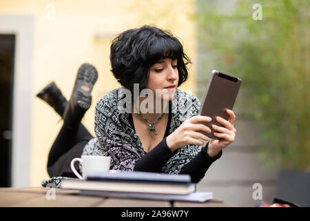 Giovane donna con il computer portatile al di fuori lavoro e giacente su di una tavola Foto Stock