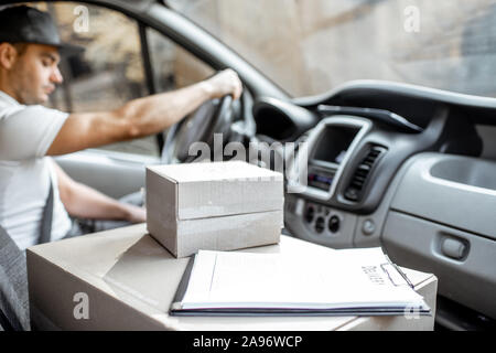 Consegna uomo alla guida di veicolo carico con pacchi sul sedile del passeggero, immagine focalizzata sulle scatole di cartone con uno spazio vuoto