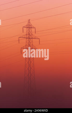 Torre di trasmissione dopo il tramonto che emergono dalla nebbia su uno sfondo arancione sky Foto Stock