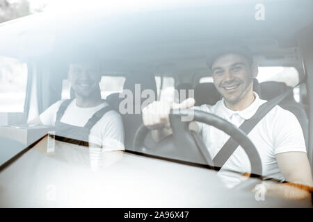 Allegra compagnia di consegna dipendenti alla guida di un veicolo da carico, consegna delle merci da un auto, vista attraverso il parabrezza Foto Stock