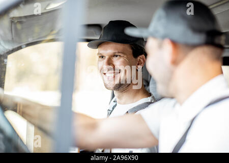 Due allegro consegna i dipendenti della società in uniforme avente fun durante la guida di un veicolo da carico, la consegna delle merci ai clienti Foto Stock