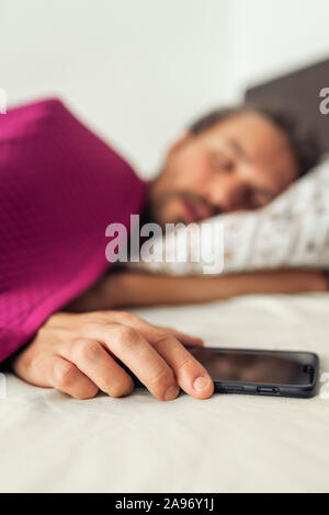 Sleeping giovane uomo bello mentre si tiene il suo telefono cellulare. Schermo del telefono è disattivato Foto Stock