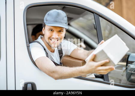 Allegra compagnia di consegna dipendenti consegna delle merci ai clienti in un veicolo da carico, bello courier guardando fuori dalla finestra di auto con un pacco