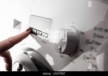 Primo piano particolare di donna di dito indice con smalto per unghie spingendo il pulsante sulla bianca e moderna macchina di lavaggio Foto Stock