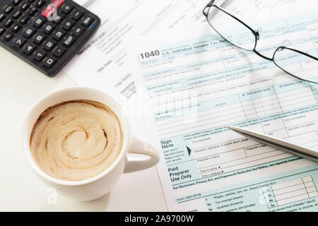 Tazza di caffè cremoso sul tavolo bianco con gli Stati Uniti di redditi forma 1040, visibile penna, calcolatrice e occhiali. Imposta, contabile, di business, finanza Foto Stock