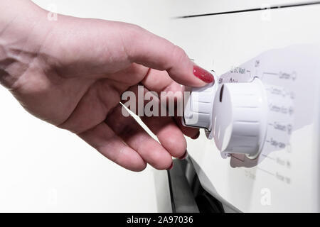 Primo piano particolare di donna di mano sinistra con unghie delle dita lucidato ruotando una manopola su bianco moderna macchina di lavaggio Foto Stock