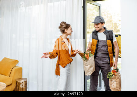 Corriere in uniforme erogazione di generi alimentari freschi a casa per un giovane client. Lo shopping online e di consegna a domicilio di concetto Foto Stock