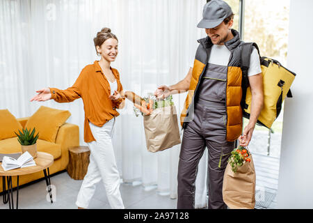 Corriere in uniforme erogazione di generi alimentari freschi a casa per un giovane client. Lo shopping online e di consegna a domicilio di concetto Foto Stock