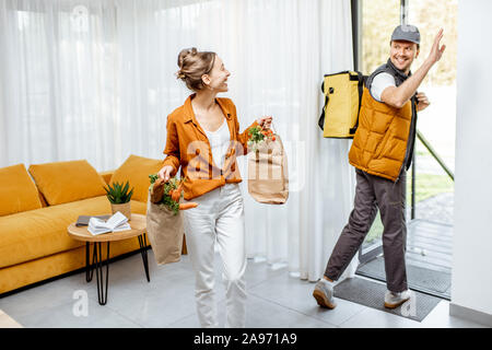 Corriere consegna generi alimentari freschi a casa per un giovane client, felice donna in piedi con acquisti con consegna uomo uscire di casa Foto Stock