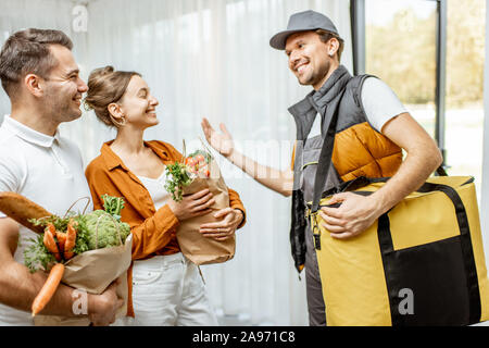 Allegro corriere in uniforme erogazione di generi alimentari freschi ad una giovane famiglia home. Lo shopping online e di consegna a domicilio di concetto Foto Stock