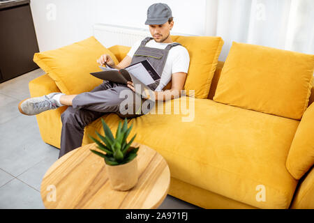 Tuttofare in workwear seduto sul divano giallo durante il riposo dopo il lavoro Foto Stock