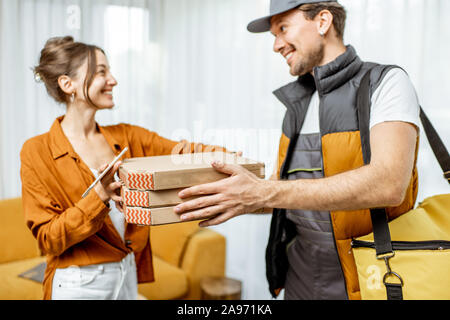 Bello corriere in uniforme garantendo la pizza con borsa termica per un client home, donna felice ricevere il suo ordine Foto Stock